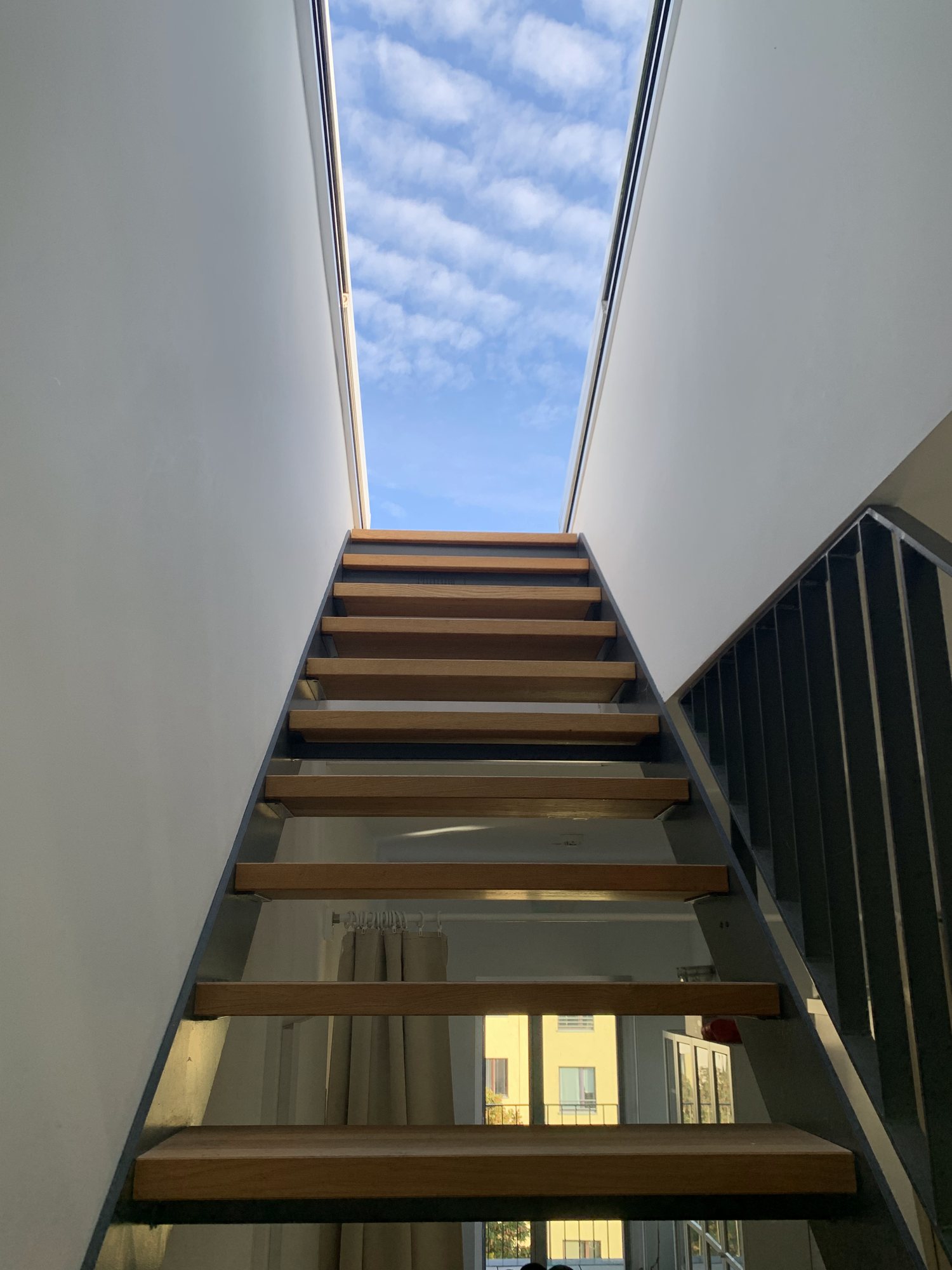 Offene Holztreppe, die zu einem Oberlicht mit blauem Himmel führt